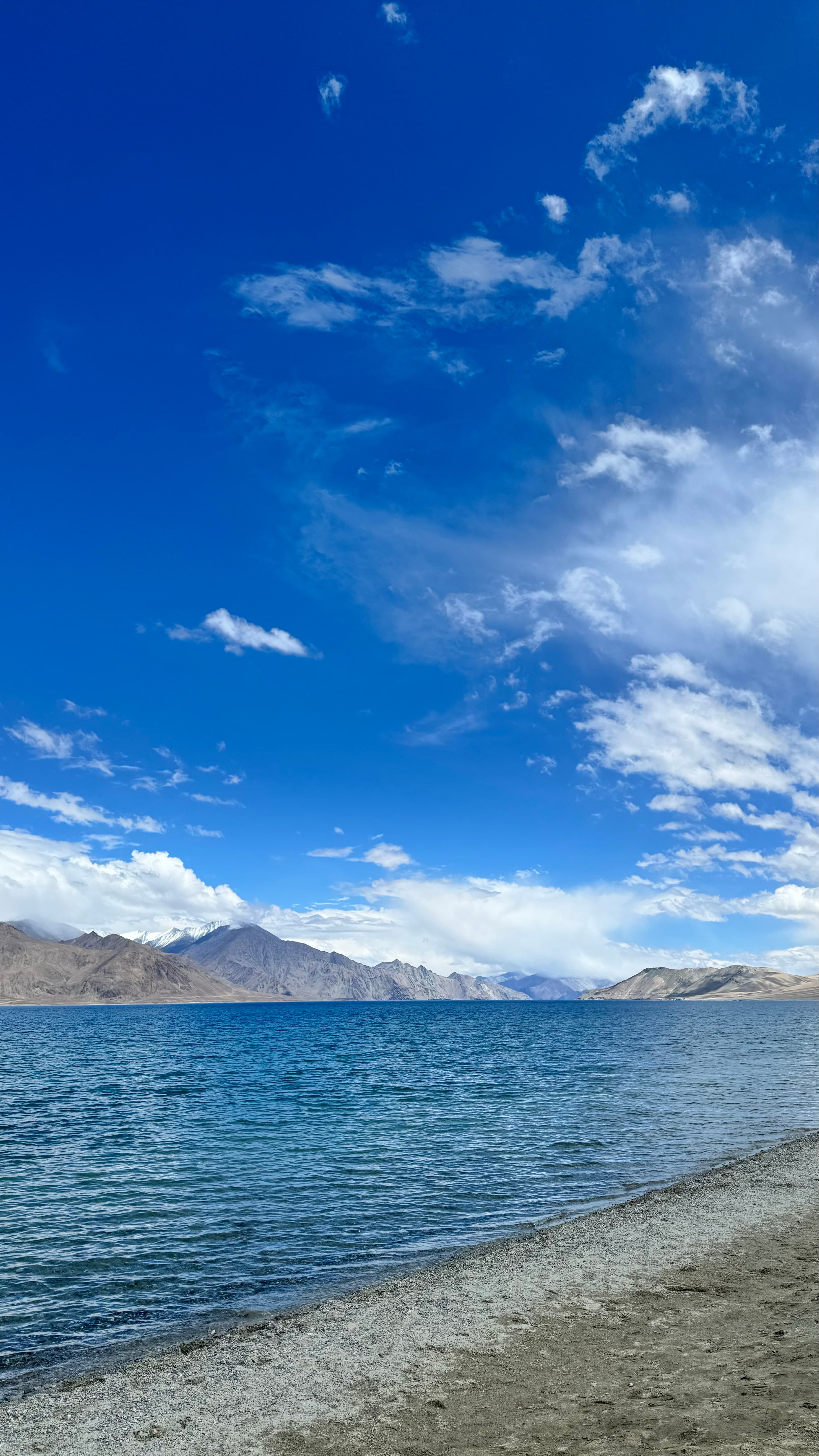 Pangong Lake with deep blue water stretching toward snow-capped mountains under an open sky