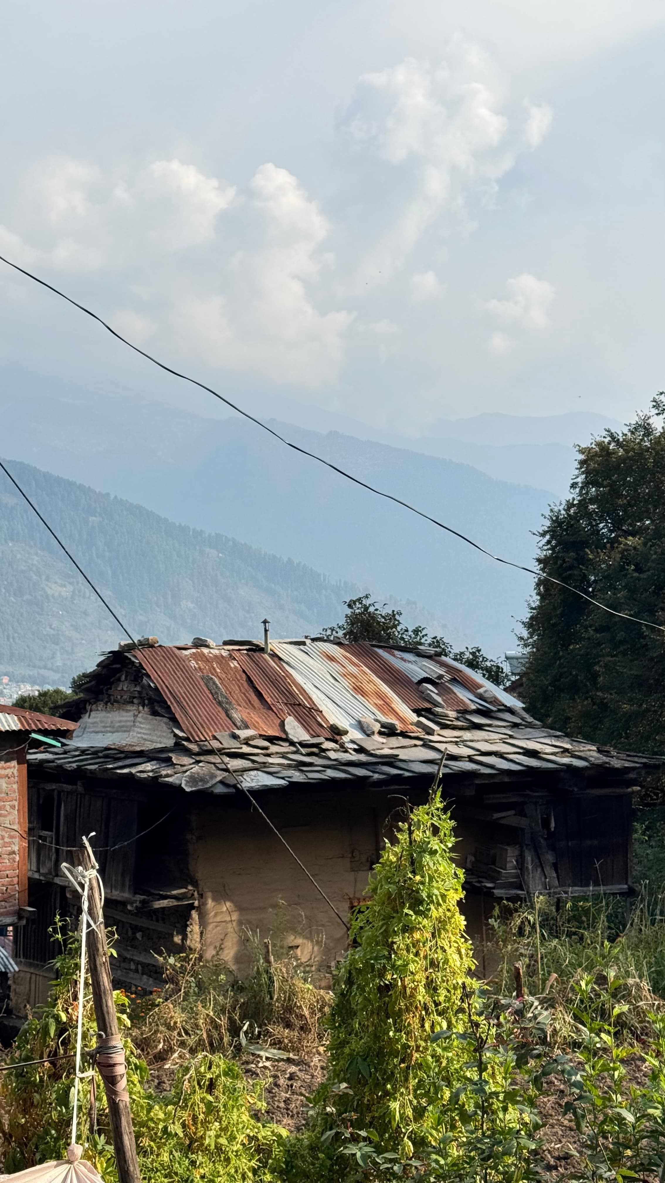 Rustic stone house with misty mountain layers behind it in Himachal Pradesh